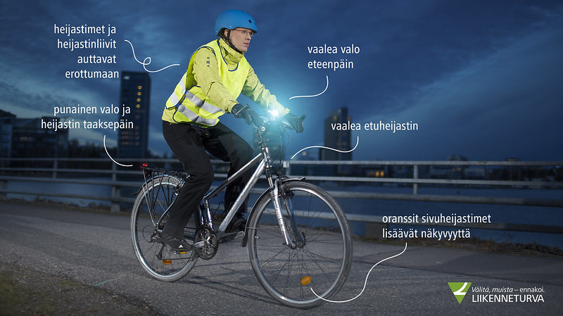 Pyöräilijä, jolla on päässä kypärä, yllään heijastinliivi, pyörässä heijastimet ja valot kunnossa.
